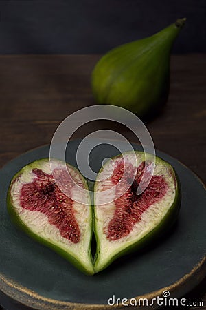 Sliced â€‹â€‹ripe figs in a round bronze aquamarine vintage plate on a wooden table under the rays of light. Stock Photo